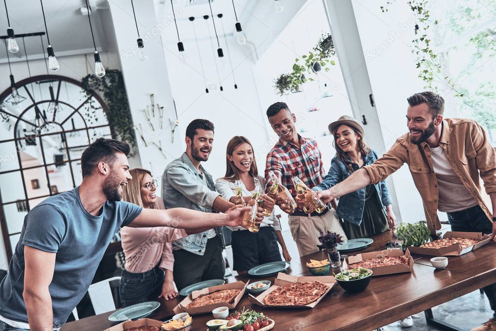 young people in casual wear toasting each other and smiling while having a dinner party