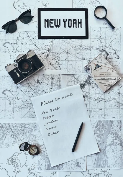 flat lay shot of world map with sunglasses, photo camera, compass, magnifying glass, paper with written checklist and passport, trip to new york