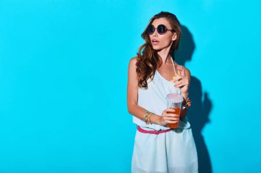 uzağa bakarak ve saman ile kokteyl içki tutan sürpriz genç kadın 