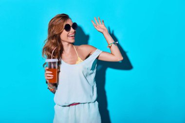 Yaz içeceği tutan gülümseyerek ve el ile sallayarak kadın