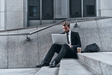 Modern teknolojiler, merdivenlerde açık havada otururken dizüstü kullanarak takım elbiseli adam kullanarak