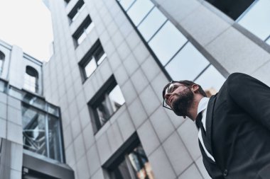 düşük açılı görünüş iyi görünümlü genç adam açık havada ofis binası, ayakta iken uzakta tam takım arıyor