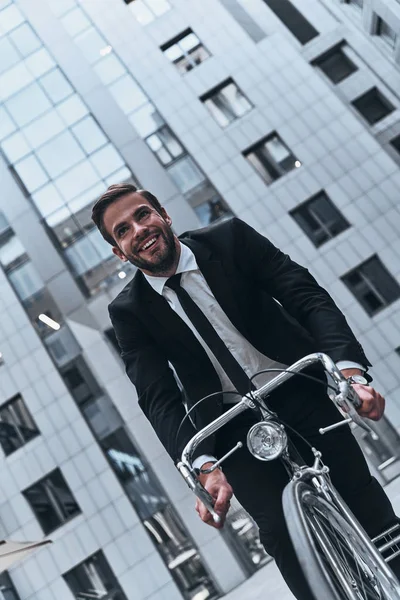 事務所ビルで自転車に乗ってスーツを着た若い男の笑みを浮かべてください — ストック写真
