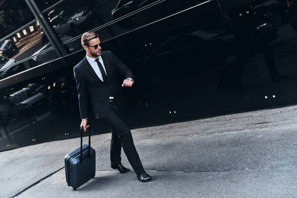 full length of young businessman in suit pulling luggage while walking outdoors