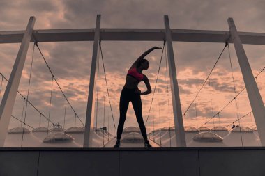 sportif genç kadının günbatımı gökyüzü, modern binanın çatı üzerinde egzersiz yapması tam uzunlukta