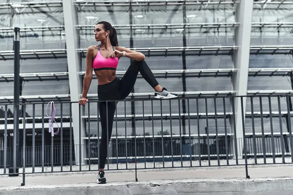 caucasian sportive woman stretching legs outdoors at railings of stadium