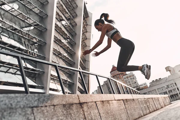 Caucasian woman in sport leggings jumping back from railings outdoors