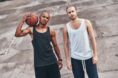 young handsome men in sports clothing looking at camera while standing outdoors with basketball ball clipart