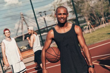 Genç Afrika adam kameraya bakarak ve arka plan üzerinde arkadaşlar basketbol topu, holding giyim spor 