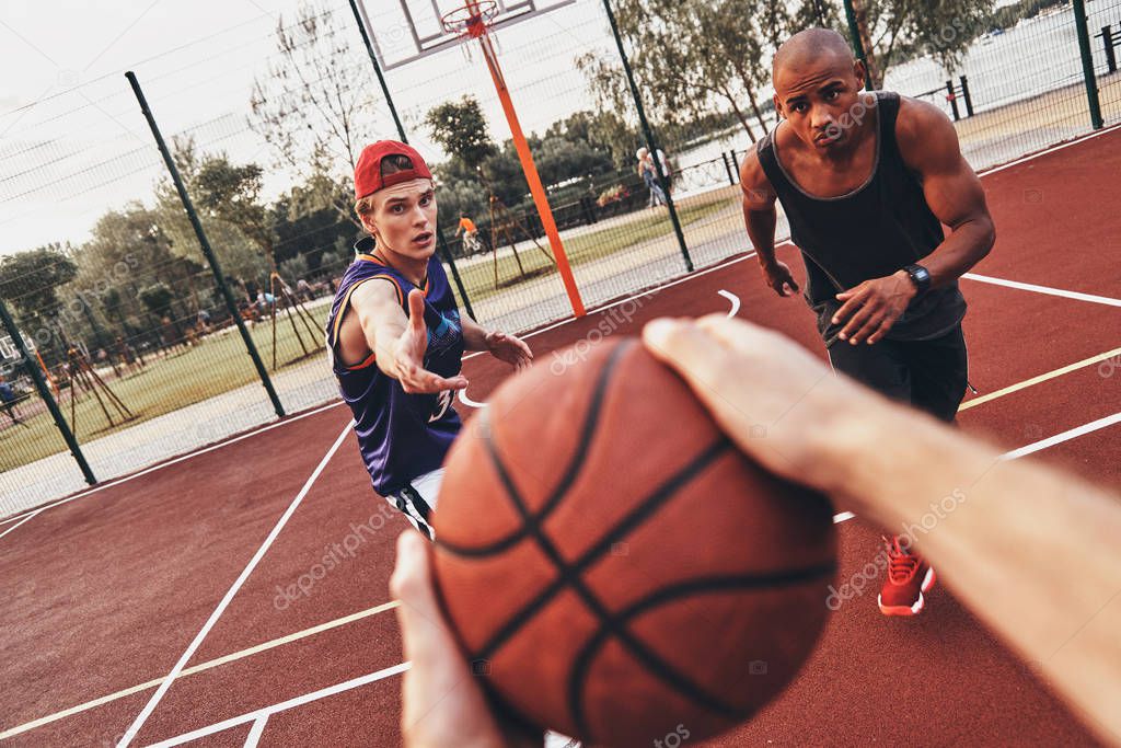 close up of man holding ball while playing basketball with friends outdoors