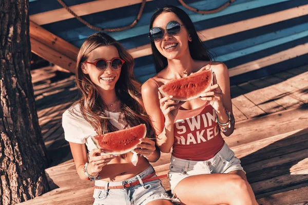 Amigos Mujeres Sosteniendo Rodajas Sandía Mientras Sienta Playa Mirando Cámara —  Fotos de Stock