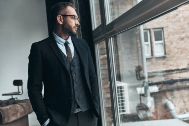 Tam takım uzak kapalı ayakta iken pencereden bakarak düşünceli adam