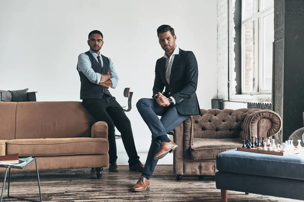Två Stiliga Män Kostymer Tittar Kameran Medan Vilar Inomhus — Stockfoto