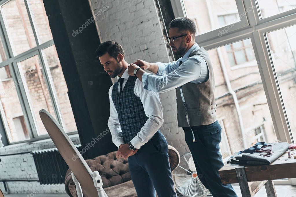 fashionable man choosing suit with help of fashion designer in boutique