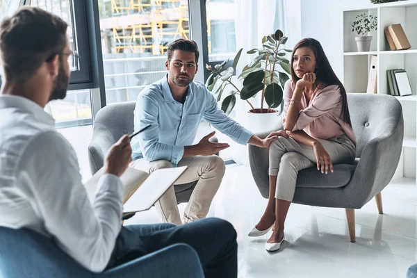 married couple talking while sitting on therapy session with psychologist