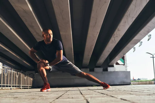 Africano Con Ropa Deportiva Estirando Las Piernas Mientras Calienta Bajo — Foto de Stock