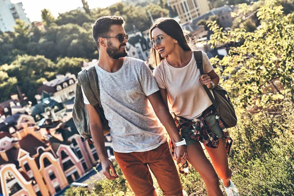 smiling Caucasian couple in casual clothing walking outdoors, city houses on background