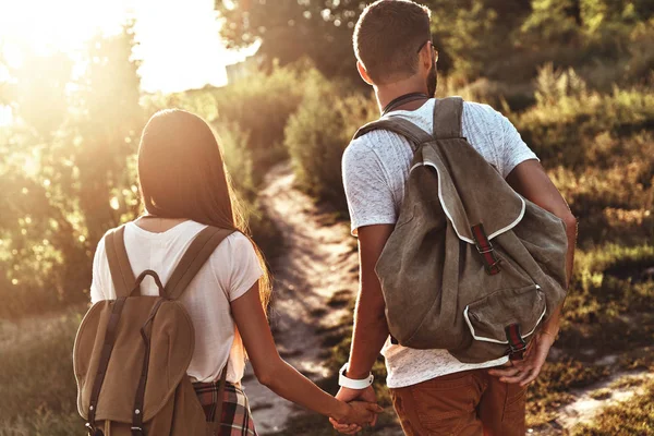 屋外に立っている間手を繋いでいるバックパックと若いカップルの背面図 — ストック写真
