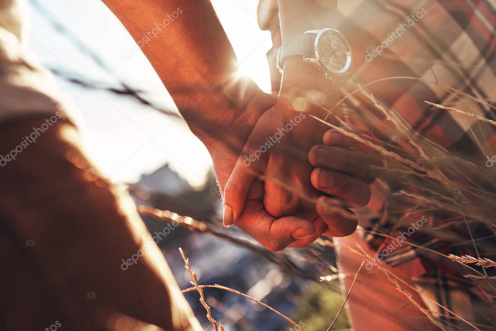 partial view of couple holding hands while standing outdoors in grass 