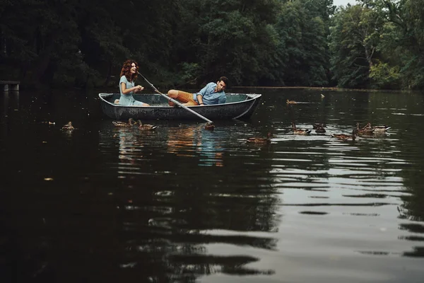 Couple feeding ducks while enjoying romantic date on lake in boat