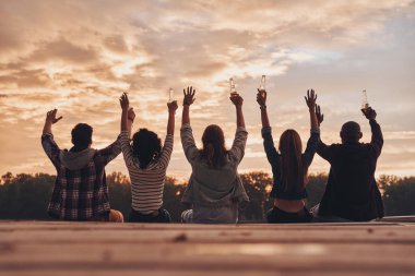 Arkadan Görünüş gençlerin iskele, günbatımı gökyüzü nehri üzerinde oturup bira şişeleri ile 