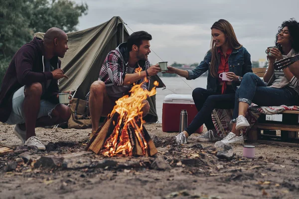 朋友坐在篝火旁 在湖边休息 用饮料挖旅行杯 — 图库照片