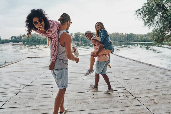 若くて美しいカップル木製の桟橋に屈託のない時間を費やして肩の女性を運ぶ男性 — ストック写真
