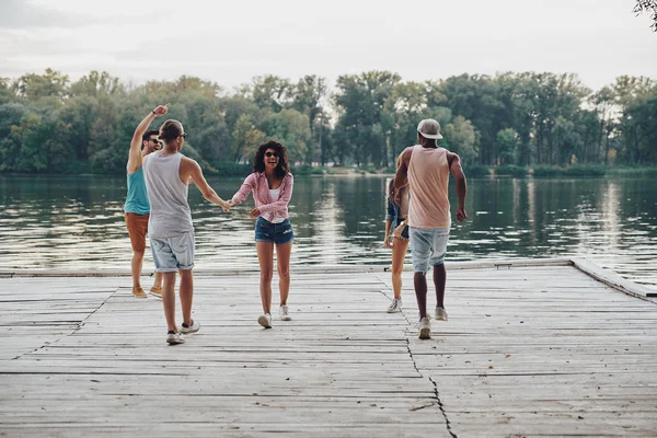 笑みを浮かべて 川で木製の桟橋の上で踊ってカジュアルな服装で若者の全長 — ストック写真