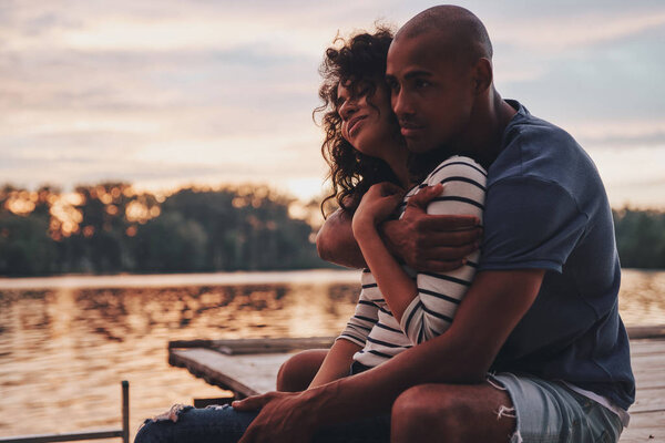 романтическая влюбленная пара, обнимающая и сидящая на пирсе у озера
 