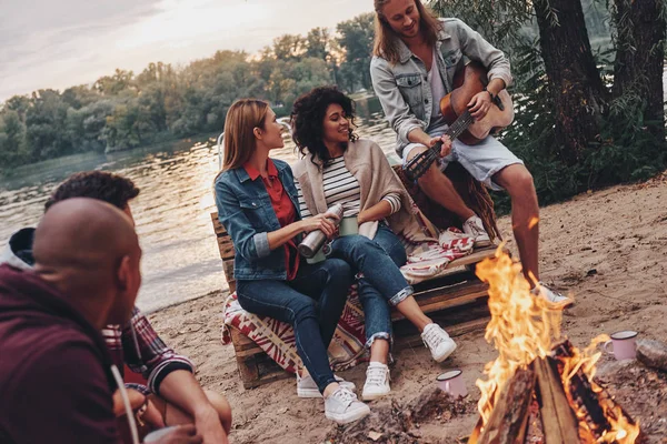 Giovani Abbigliamento Casual Godendo Campeggio Vicino Lago Tramonto Uomo Suonare — Foto Stock