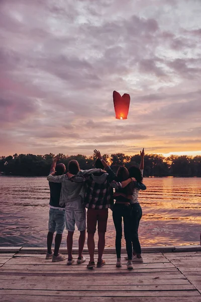 最佳朋友在木码头和飞行红色心脏灯笼气球在日落天空 — 图库照片