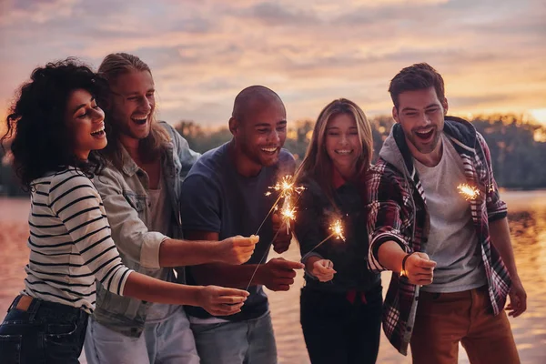 Friends Smiling Holding Sparklers While Standing Pier Sunset — Stock Photo, Image