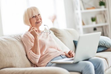 evde kanepede oturan ve dizüstü çök tutan yaşlı düşünme kafkas kadın 