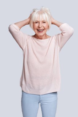 ışık kazak ve Studio gri arka plan, poz ve kafasına geri el ele tutuşarak kısa gri saç beyaz kadın gülüyor