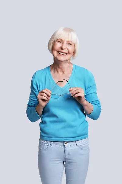 老年妇女短灰色头发摆在灰色背景在工作室和穿着明亮的蓝色毛衣 — 图库照片