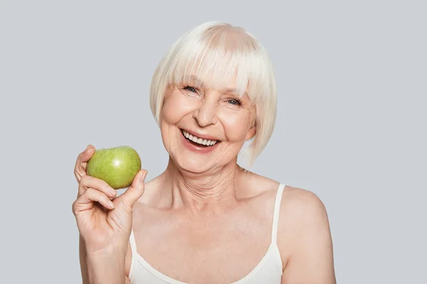 Sonriente Mujer Mayor Sosteniendo Manzana Verde Pie Sobre Fondo Gris — Foto de Stock