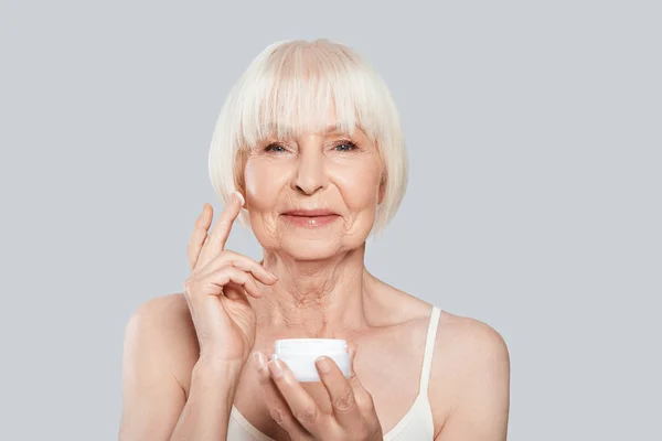 Beautiful Senior Woman Applying Beauty Cream Face While Standing Grey — Stock Photo, Image