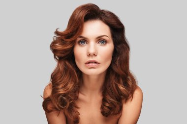 baştan çıkarıcı genç kadın esmer dalgalı saçlı gri arka plan poz ve kameraya bakıyor