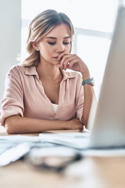 dizüstü bilgisayar ve kağıtları ile masada otururken çeneme el tutmak düşünceli genç kadın 