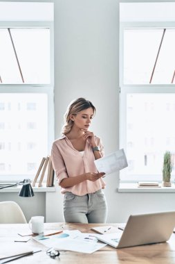 dizüstü bilgisayar ile masada duran belge kağıt bakarak düşünceli kadın 