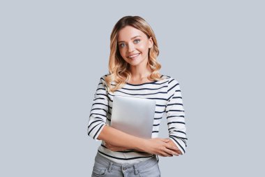 gülümseyen ve kamera, dijital tablet ellerde ile gri arka plan ayakta bakmak çekici genç kadın 