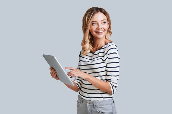 微笑的年轻妇女看着远 站在灰色背景与数字平板电脑在手 — 图库照片