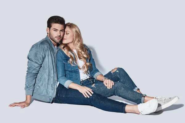 Belo Jovem Casal Roupas Jeans Sentado Chão Fundo Cinza — Fotografia de Stock