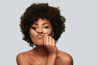 gömleksiz kameraya bakarak ve kıvırcık saçlı oynarken Studio flört Afrikalı kadın portresi 