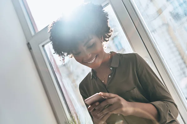 Atractiva Mujer Africana Joven Mensajes Texto Teléfono Inteligente Sonriendo Mientras —  Fotos de Stock