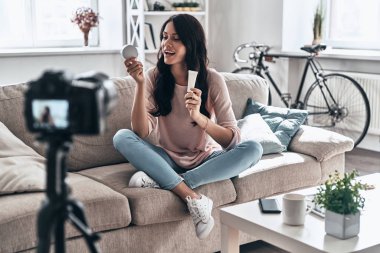 Sosyal medya video yapma ve güzellik ürünleri ile kanepede oturan kadın bazen gülümseyerek