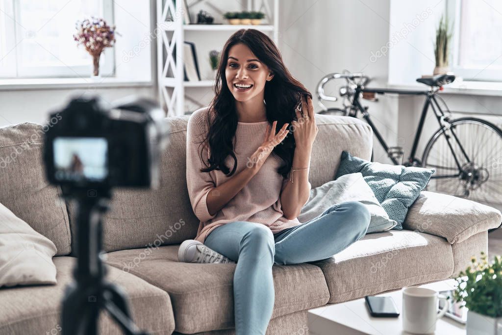 female vlogger making social media video while sitting on sofa in living room