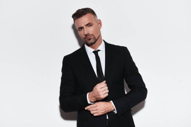 Kendine güvenen adam kol ayarlama ve kamera beyaz arka plan karşı dururken bakarak tam takım