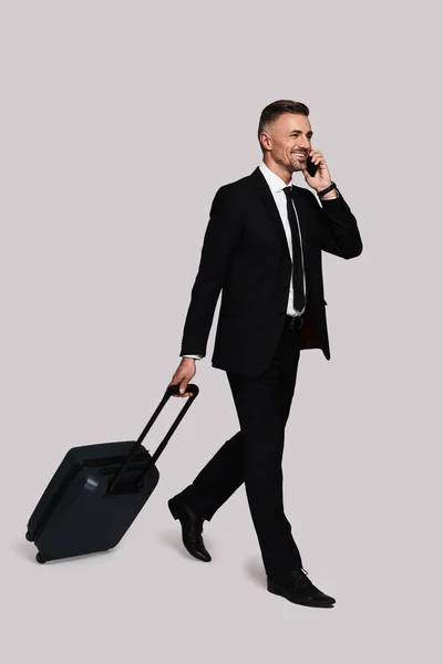 トラベル バッグとスタジオで歩きながら携帯電話で話している黒い服を着て良い探しているビジネスマン — ストック写真