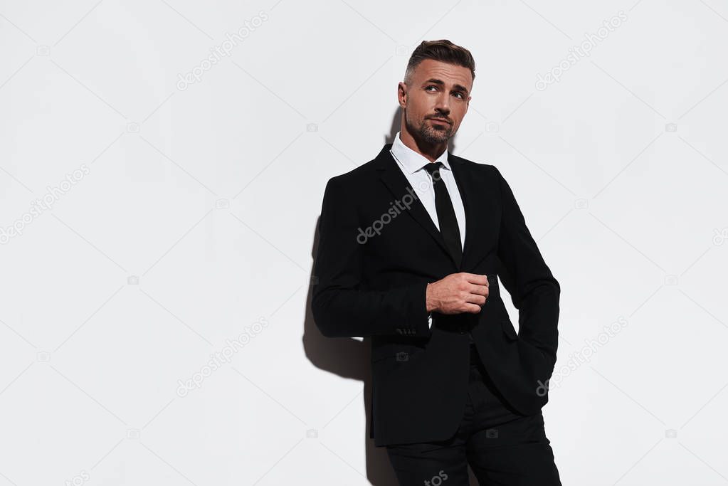 Thinking man in full suit keeping hand in pocket and looking away while standing against white background